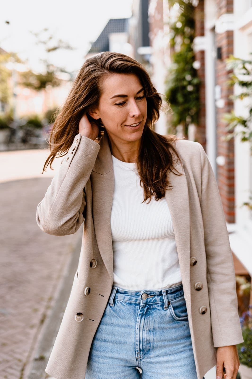Manon de Jong kijkt opzij en houdt een hand bij haar haar, buiten in een straat.